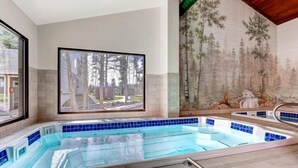 Una piscina con vistas a árboles a través de un amplio ventanal, una pared de azulejos con un mural de un bosque y un techo de madera.