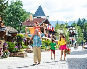 Une famille se promène sur une place, avec des immeubles et des boutiques en arrière-plan.