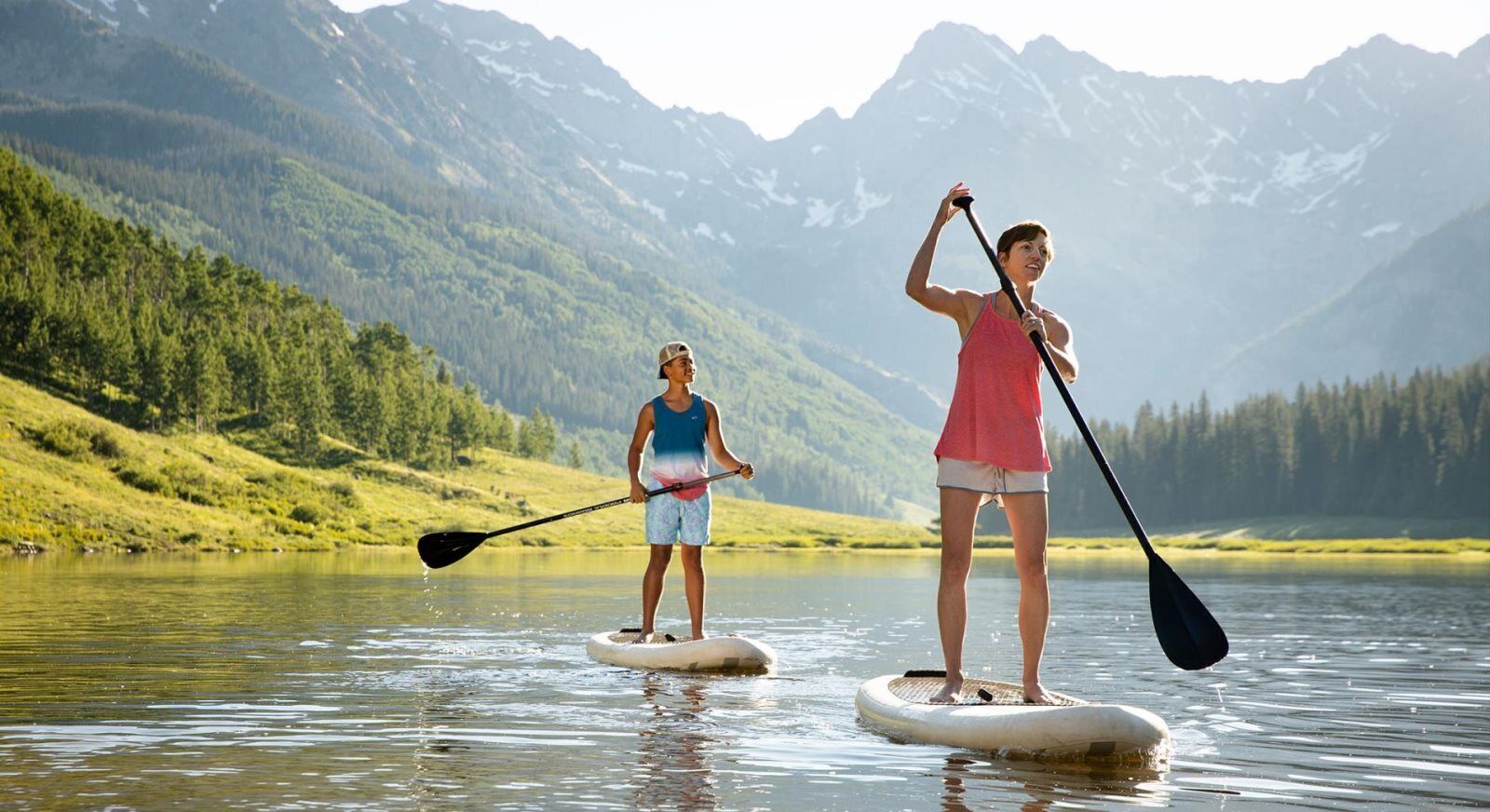 Due persone che fanno paddleboard su un lago calmo, circondato da montagne.