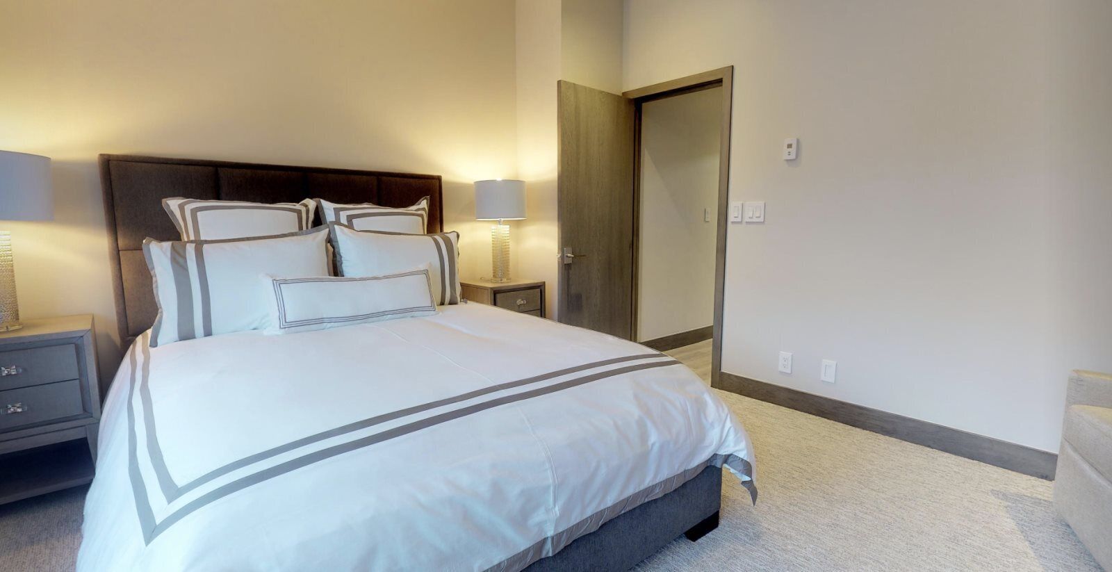 A neatly arranged hotel room with a large bed, bedside lamps, a nightstand, and a door.