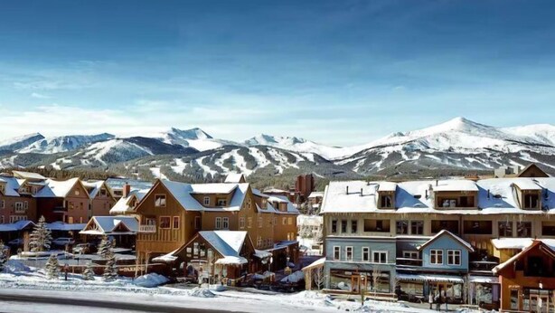 Un pueblo cubierto de nieve con edificios de madera y una montaña al fondo.