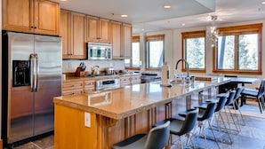 A modern kitchen with stainless steel appliances, wooden cabinets, a large island with bar stools, and large windows offering a view of the outdoors. - 4 Bedroom Condo (Keystone)