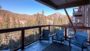 A balcony with two chairs and a table, overlooking a mountainous landscape with trees and buildings. - 4 Bedroom Condo (Keystone)