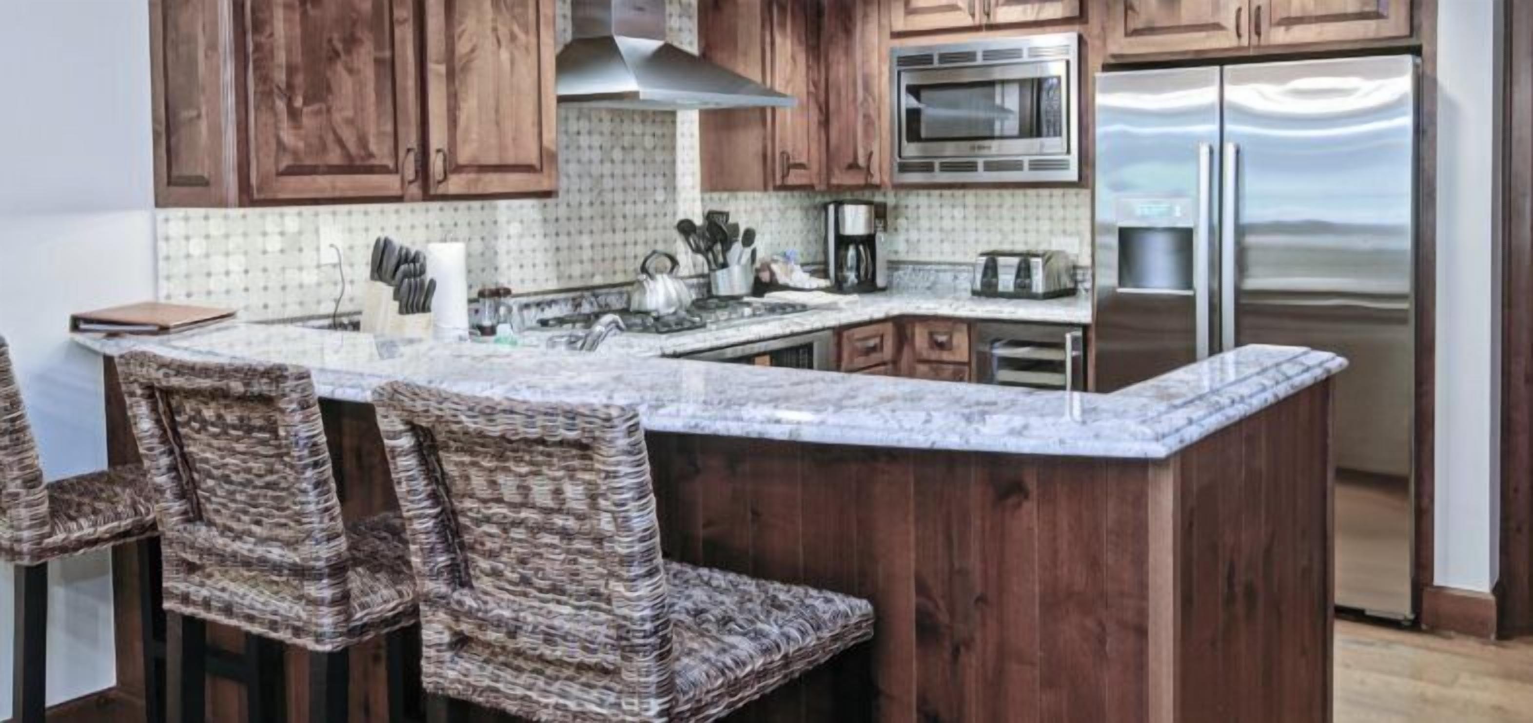A kitchen with wooden cabinets, a stainless steel refrigerator, a microwave, and a granite countertop.