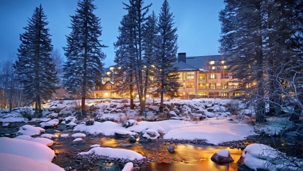 A lodge with a river flowing through a snowy landscape, surrounded by tall evergreen trees. - Guest Room - 1 King (Vail)