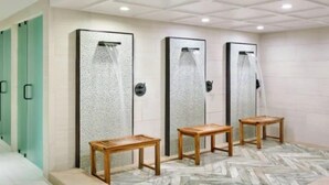 A restroom with three shower stalls, each with a glass door and a showerhead. There are wooden benches in front of the stalls. - Guest Room - 1 King (Vail)