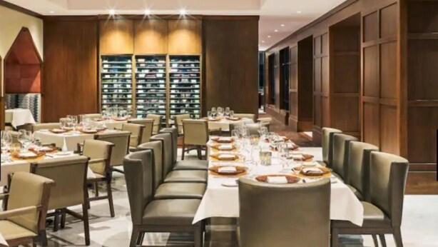 A formal dining room with multiple tables set for service, a large wine rack in the background, and a modern interior design. - Guest Room - 1 King (Vail)