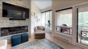 Una sala de estar moderna con chimenea de piedra, televisor de pantalla plana, un sofá y un amplio ventanal con balcón.