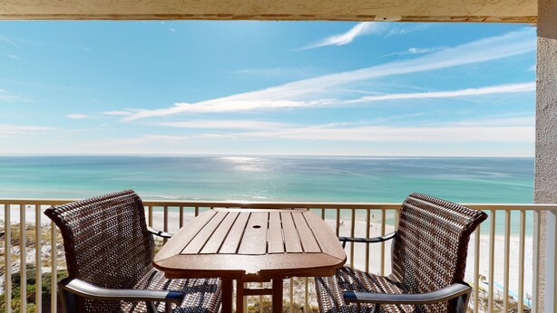 A wooden table and two wicker chairs on a balcony with a view of the ocean. - Beach Manor 1110 (Miramar Beach)