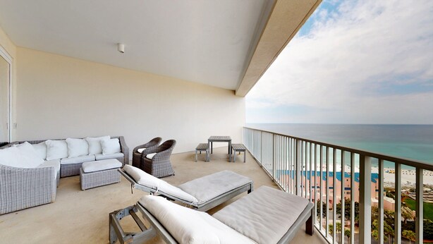 A balcony with wicker furniture, a small table, and a view of the beach. - Tides 1410 (Miramar Beach)