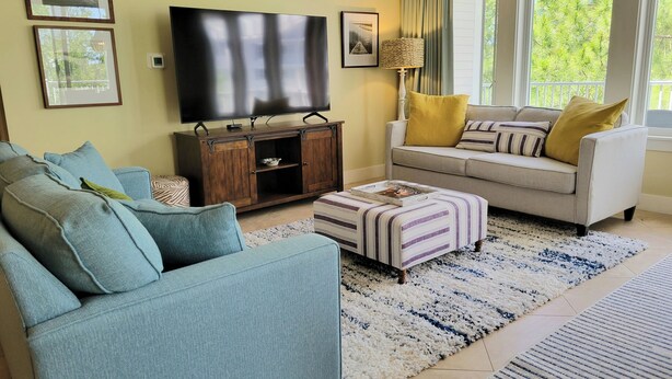A living room with a sofa, ottoman, and a television on a wooden cabinet. - Lasata 3401-3403 Lockout (Miramar Beach)