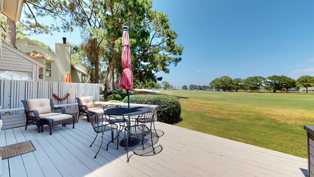 A deck with outdoor furniture, including chairs and a table, overlooking a grassy area with trees. - Fairways 296 (Miramar Beach)