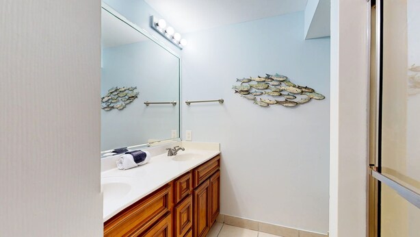 A bathroom with a white sink, wooden cabinets, a glass shower enclosure, and decorative fish wall art. - Beach Manor 0111 (Miramar Beach)