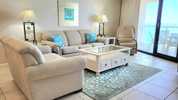 A living room with a sofa, coffee table, and armchairs, a large window with curtains, and artwork on the wall. - Beachside II 4302 (Miramar Beach)