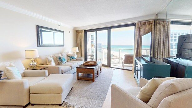 Ein Hotelzimmer mit großem Balkon, einer Sofagruppe, einem Couchtisch, einem Fernseher und einem Schreibtisch mit Computer.