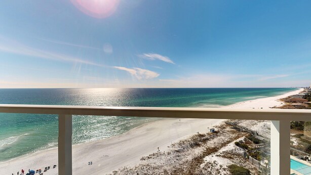 A beach view from a balcony with a clear sky, ocean, and a distant shoreline with buildings. - Beachside II 4338 (Miramar Beach)