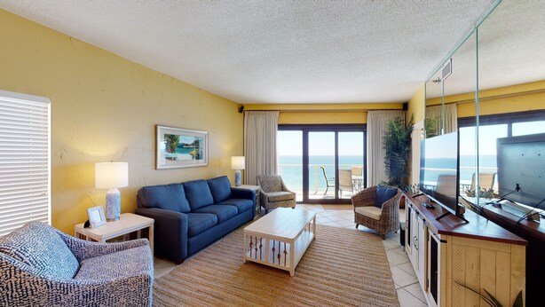 Un salon comprenant un canapé, des fauteuils, une table basse, un téléviseur et une vue sur la mer grâce à de grandes fenêtres.