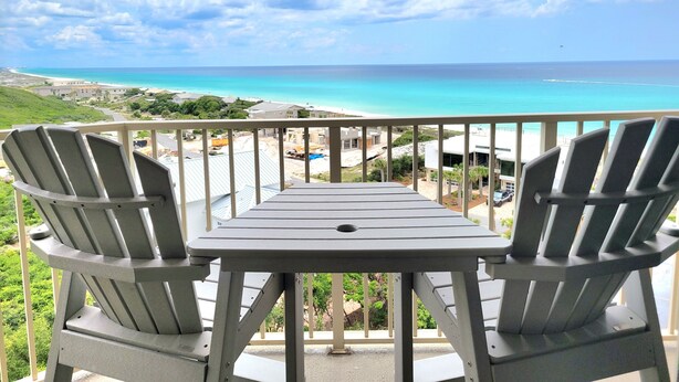 A balcony with two Adirondack chairs and a table overlooking a beach and ocean. - Beach Manor 0802 (Miramar Beach)