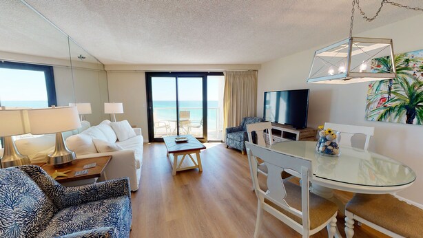 Un soggiorno moderno con divano, poltrone, tavolo da pranzo, televisione e un balcone con vista sul mare.