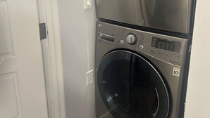 A stacked washer and dryer unit in a corner with a white door adjacent to it. - Basement suite with full kitchen  (Airdrie)