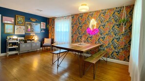 A dining area with a wooden table and benches, a small kitchenette, and a colorful floral wallpaper.