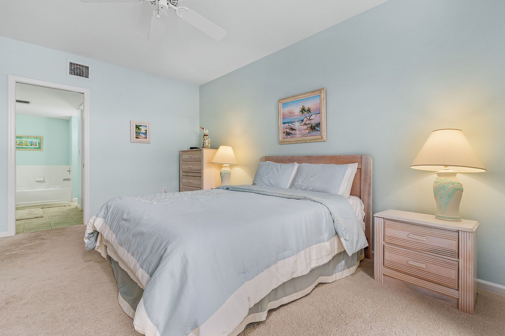 Quarto com cama, luminárias de cabeceira, mesa de cabeceira, um quadro e porta para o banheiro.