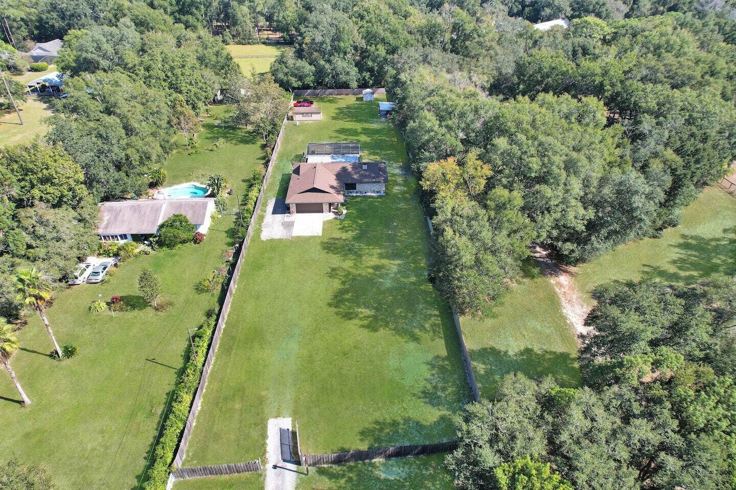 An aerial view of a residential property with a large lawn, a swimming pool, and a detached house with a garage.