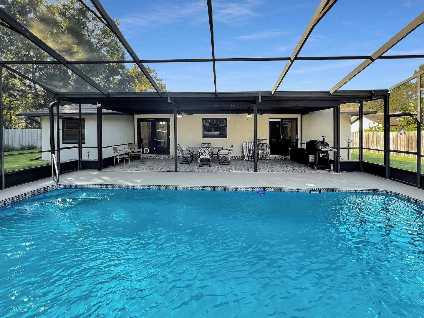 A covered swimming pool with a patio area, including seating and a barbecue.