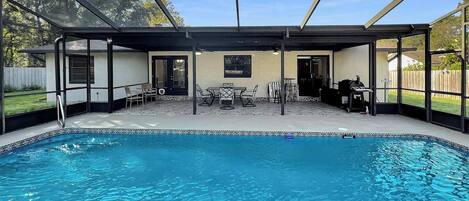 A covered swimming pool with a patio area, including seating and a barbecue.