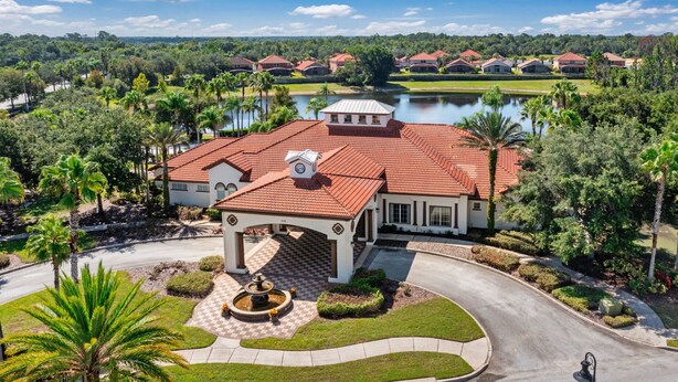 A large, single-story house with a red-tiled roof, a central courtyard with a fountain, and a view of a lake and surrounding greenery.