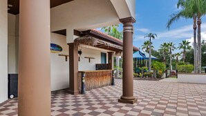 A checkered outdoor area with a covered seating area, palm trees, and a clear sky.