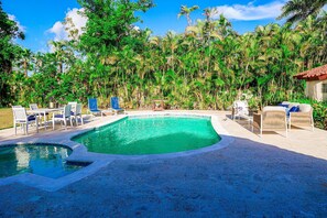 Une piscine entourée d’une végétation luxuriante, avec des chaises longues et une table à proximité.