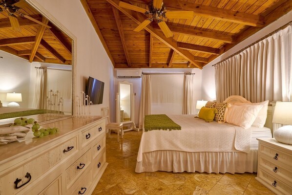 Une chambre avec un plafond en bois, un grand lit avec de nombreux oreillers, une coiffeuse avec un miroir et un téléviseur.