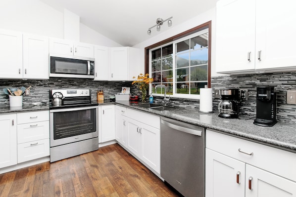 A modern kitchen with white cabinets, a stainless steel microwave, an oven, a dishwasher, and a coffee maker.