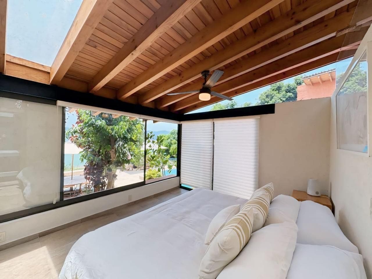 A bedroom with a large bed, a ceiling fan, and a view of the outdoors.