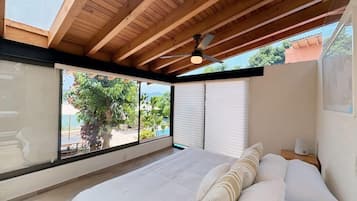 A bedroom with a large bed, a ceiling fan, and a view of the outdoors.