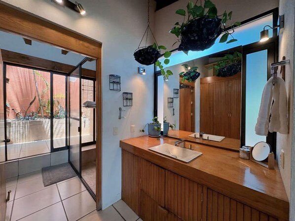 A modern bathroom with a wooden vanity, a large mirror, and potted plants.