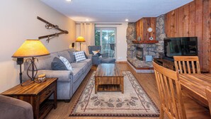 A cozy living room with a stone fireplace, a television, and a comfortable seating area with a sofa and chairs. - Ideal Location with 2 Queens + 2 Twins, Hot Tubs, Pool, & Clubhouse (Winter Park)