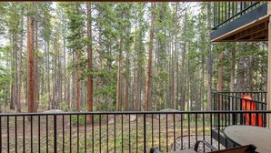 A balcony with a view of a dense forest. There are two chairs and a table on the balcony. - Ideal Location with 2 Queens + 2 Twins, Hot Tubs, Pool, & Clubhouse (Winter Park)