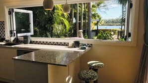 A kitchen with a large window, a granite countertop, and a view of a tropical landscape. - Stunning River front Cottage with pool (Dunbogan)
