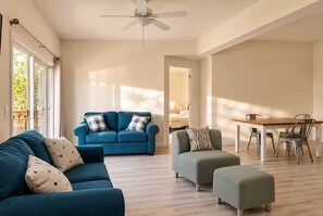 Una sala de estar con un sofá azul, un sillón gris y una mesa de comedor con sillas.