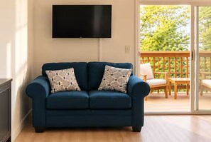 A blue sofa with patterned cushions, a flat-screen TV on the wall, and a view of a wooden deck with outdoor furniture. - Executive Suite Midtown (Wilmington)