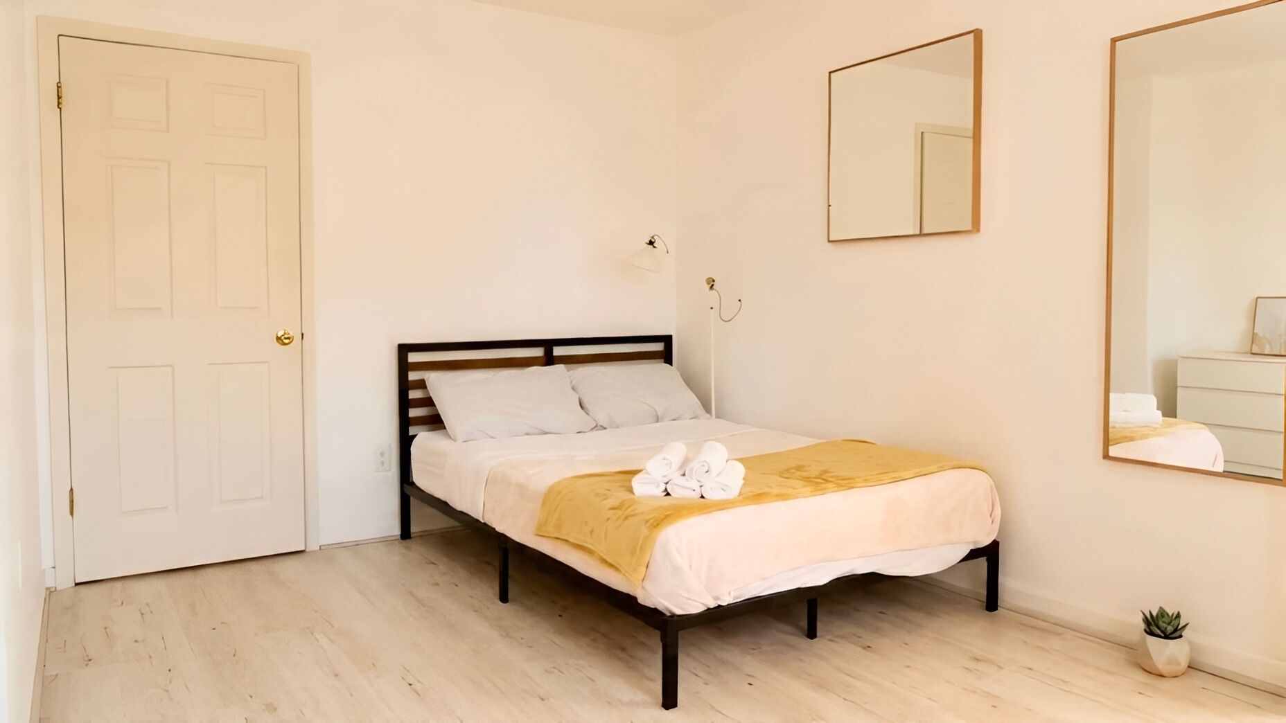 Ein Schlafzimmer mit einem Bett, einer Tür, einem Spiegel und einer kleinen Pflanze.