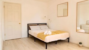 Un dormitorio con cama, una puerta, un espejo y una planta pequeña.