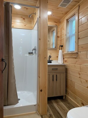 A wooden cabin bathroom with a shower, sink, and mirror.