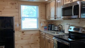 A kitchen with wooden cabinets, a stainless steel refrigerator, a microwave, and an oven. - MAPLE COTTAGE - Lakefront on Thayer Lake in Alden with WiFi, AC (Alden)