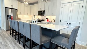 A modern kitchen with white cabinets, a stainless steel refrigerator, a microwave, and a large island with bar stools. - Built in 2024: 2100SF, 4-BR, 4-full-BA pet-friendly house in marvelous Apex (Apex)