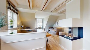 A modern kitchen with a central island, a built-in fireplace, and a dining area with a view of the living room. - Willkommen in Unserer Inselsuite! - Domizil Budersand 34 (Hörnum (Sylt))