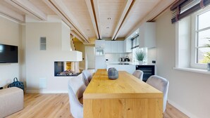 A modern kitchen with white cabinets, a wooden dining table, and a built-in stove. - Willkommen in Unserer Inselsuite! - Domizil Budersand 34 (Hörnum (Sylt))