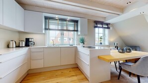 A modern kitchen with white cabinetry, a wooden countertop, and a dining area with a table and chairs. - Willkommen in Unserer Inselsuite! - Domizil Budersand 34 (Hörnum (Sylt))